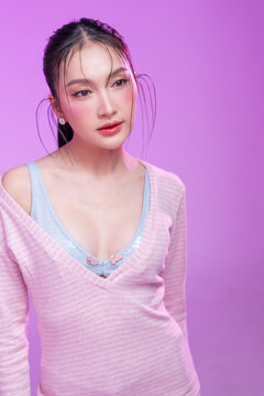 Beautiful young Asian woman with glowing skin and trendy wet hair look posing against a pastel pink background; elegant fashion portrait showcasing skincare, facial treatment, and Gen Z aesthetic.