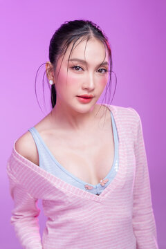 Beautiful young Asian woman with glowing skin and trendy wet hair look posing against a pastel pink background; elegant fashion portrait showcasing skincare, facial treatment, and Gen Z aesthetic.