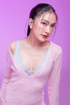 Beautiful young Asian woman with glowing skin and trendy wet hair look posing against a pastel pink background; elegant fashion portrait showcasing skincare, facial treatment, and Gen Z aesthetic.