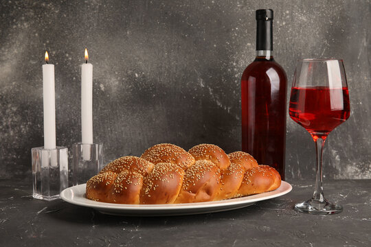 Traditional challah bread with wine and burning candles on grey grunge table. Shabbat Shalom