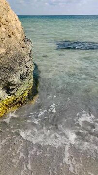 Sea Waves Crashing on Sand Near Mossy Coastal Rock