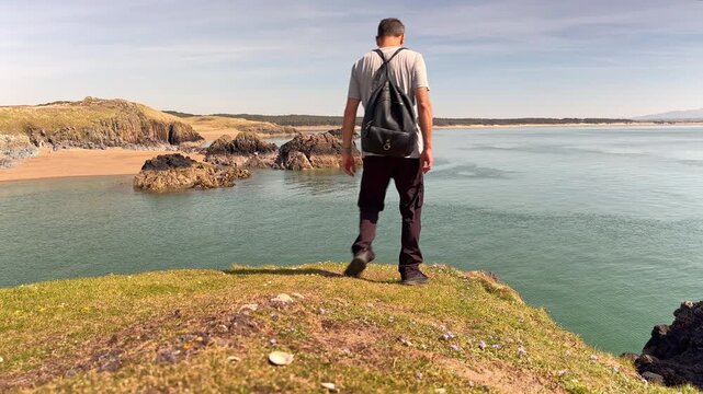 Hiker on a grassy cliff overlooking Pilot&rsquo;s Cove on Llanddwyn Island, Isle of Anglesey, Wales, United Kingdom