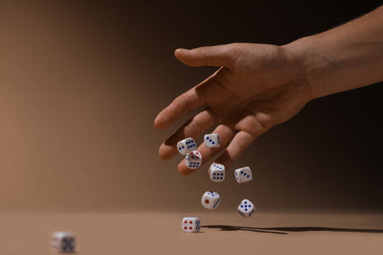 Male hand throwing game dices on beige background, closeup