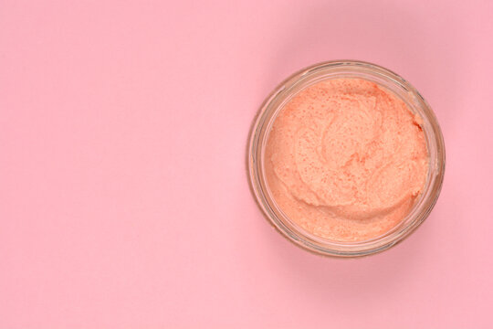 Top view of a creamy pink salmon and fish roe spread in a clear glass jar placed on a matching pink background