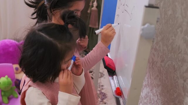 Little girls write on whiteboard together while playing school at home, learning numbers and practicing skills, showing teamwork, early education, childhood development and interactive learning