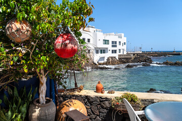 Terrace with plants and fishing floats beside white house at lava coast overlooking turquoise Atlantic water under clear blue sky in Punta Mujetres, Lanzarote © EKH-Pictures