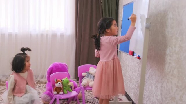 Little girls playing school at home, one child writing on whiteboard while another watching, role play education game, early learning activity, toys around, childhood development indoors