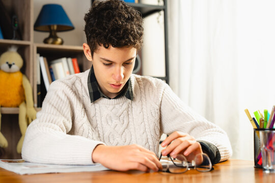 Teenage boy studying at desk with focused expression and school homework