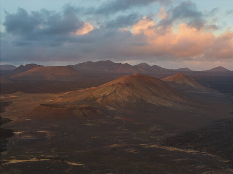 Aerial view of volcanic cones and craters in a desolate lava field under a dramatic cloudy sky at sunset Lanzarote, Canarias, Spain.
