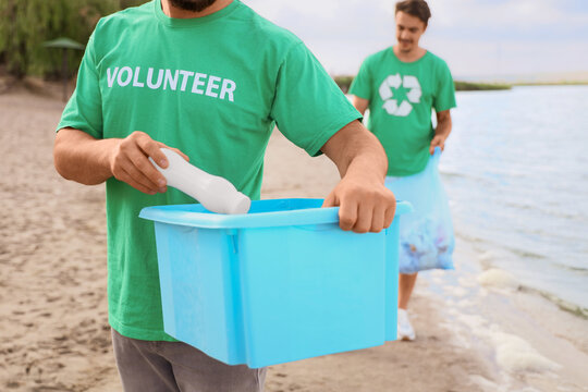 Male volunteer throwing plastic bottle into trash bin on beach. World Oceans Day