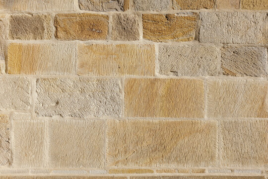 Historic sandstone ashlar wall with bush-hammered texture in warm golden tones