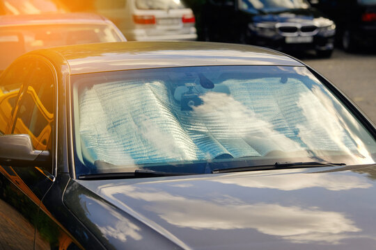 Parked black car with folding silver sunshade covering windshield, effective solution for reducing cabin temperature, blocking harmful uv radiation during hot sunny weather in outdoor parking