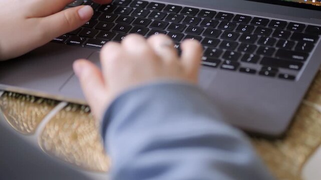 Hands typing on laptop keyboard. Fingers move across dark keys. One hand wears ring. Device rests on patterned surface. Close-up shot of work in progress