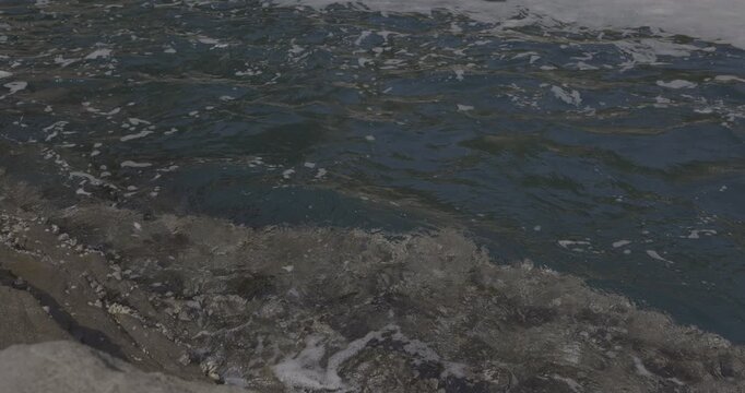 Close-up slow motion of clear ocean water splashing against coastal rocks