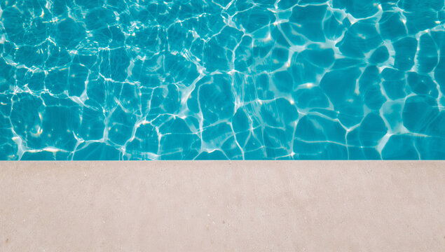 Close-up view of sparkling blue water surface with sunlight reflections and poolside edge