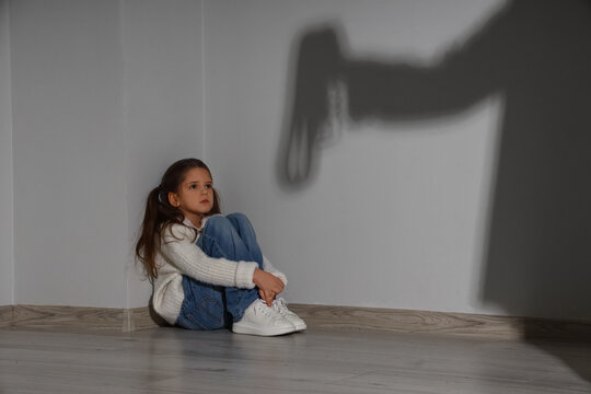 Scared girl and silhouette of her father with belt on light wall. Domestic violence concept