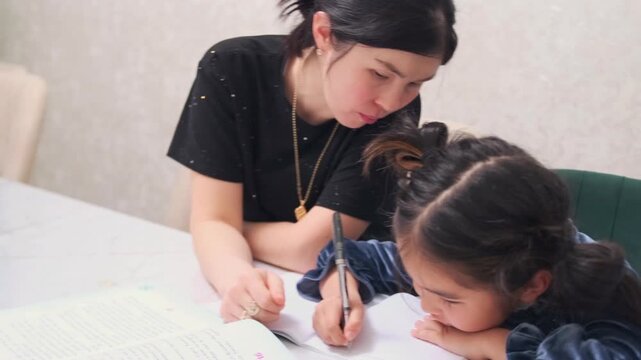 Young Asian girl shows frustration and refusal while doing homework with mother at home, emotional learning struggle, stress, resistance to studying, parenting challenge and education difficulty