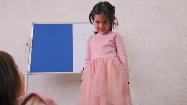 Confident little girl stands with hands on hips acting as strict teacher during play school at home, showing authority, attitude and leadership, childhood behavior and role play learning concept