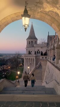Couple enjoys a romantic stroll at Fishermans Bastion in Budapest, Hungary, as the sun sets. Stunning views and intricate architecture create a perfect holiday atmosphere for travelers.