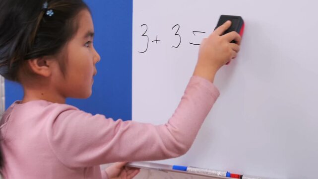 Young Asian girl erasing math equation on whiteboard at home, correcting mistake, learning process, education concept, problem solving, school practice, focused child study indoors