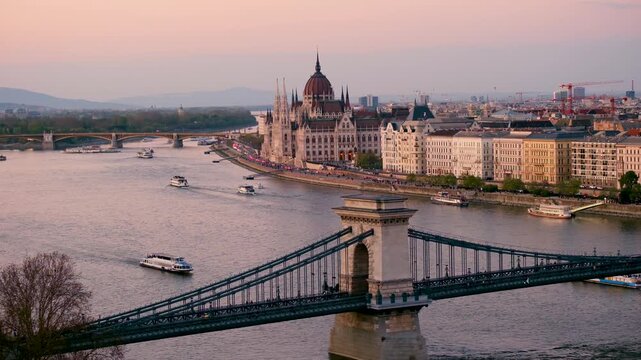Golden hues illuminate the skyline of Budapest as the sun sets over the Danube River. The iconic Chain Bridge connects stunning architecture, creating a perfect travel destination for explorers.
