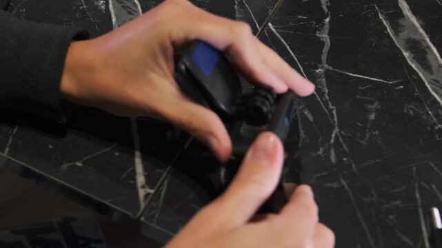 hands attaching clip mount to action camera close-up on table, tightening connector and securing device for filming, practical setup process for content creation and equipment preparation