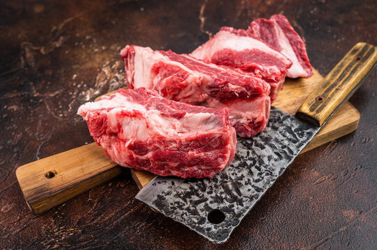 Fresh uncooked beef ribs pieces with bone and fat on cutting board.