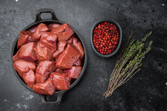 Raw lamb liver pieces in cast iron pan with thyme, mutton organ meat ingredient for cooking and traditional recipes