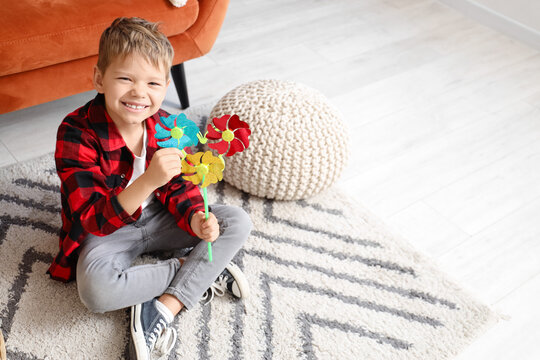 Cute little boy with toy windmill sitting on floor at home