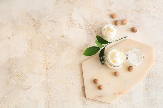 Glass jar with shea butter and nuts on grunge background