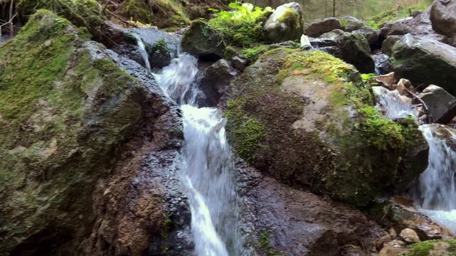 Cinematic drone pan shot from left to right across a series of small, mossy mountain waterfalls, cascading stream in a lush forest, peaceful nature scene.