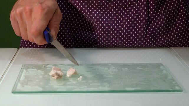 Male hands cutting cooked chicken breast fillet on glass cutting board in kitchen, front view close-up. Food preparation process for meal, slicing boiled poultry meat, healthy protein cooking