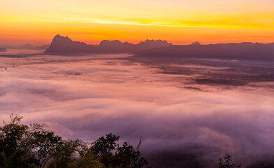 Naklejka premium Phu Kradueng National Park sunrise. Misty landscape over mountains at dawn. Thailand's natural beauty. Golden sunlight breaking through clouds.