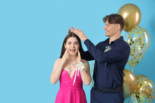 Young man crowning his prom date on blue background