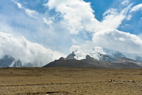 A towering snow-laden Himalayan mountain in North Sikkim above a vast rocky plateau and cloudy sky.