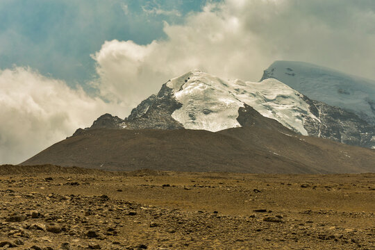A snow-clad mountain in North Sikkim dominates a rugged high-altitude landscape under scattered clouds.