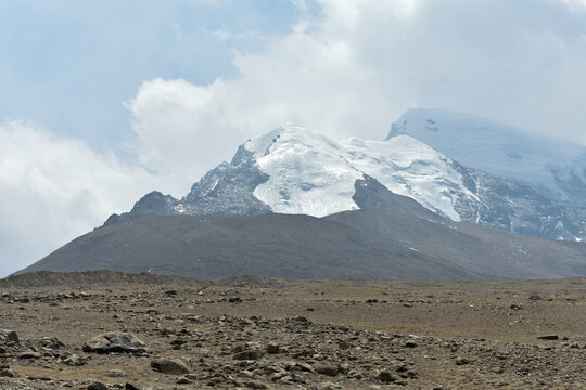 Snow-capped Himalayan peak in North Sikkim rising above a barren high-altitude plateau under blue sky and drifting clouds, showcasing rugged terrain.