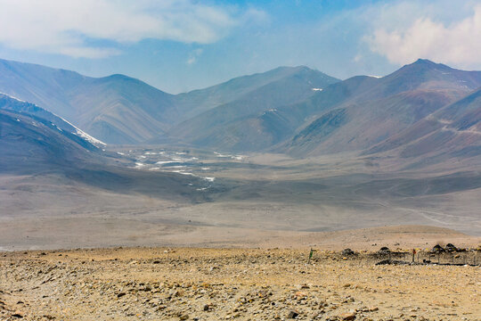 Vast high-altitude Himalayan valley with winding streams, barren terrain, and layered mountain ranges under a hazy blue sky in North Sikkim.