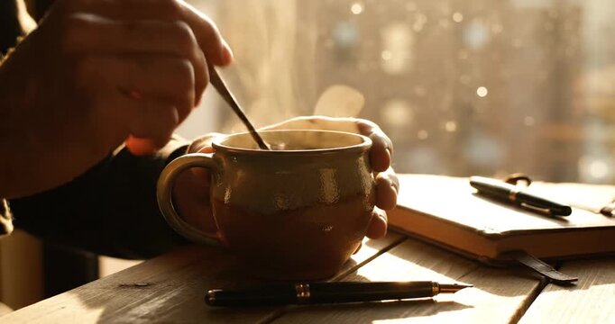 A person stirring a warm beverage in a cozy setting with sunlight streaming through a window