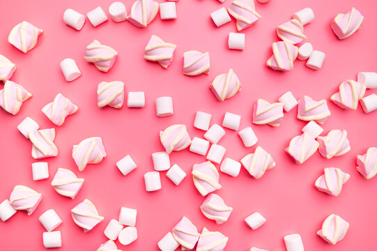 Scattered marshmallows on pink background flat lay top view. Sugar candies, sweet abstract background. Delicious dessert, pastel soft shades
