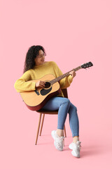 Obraz premium Young African-American woman playing acoustic guitar on pink background