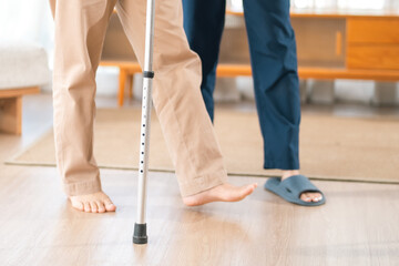Naklejka premium Caregiver with Asian senior patient, cane walking foot leg balance rehabilitation indoor person support therapy