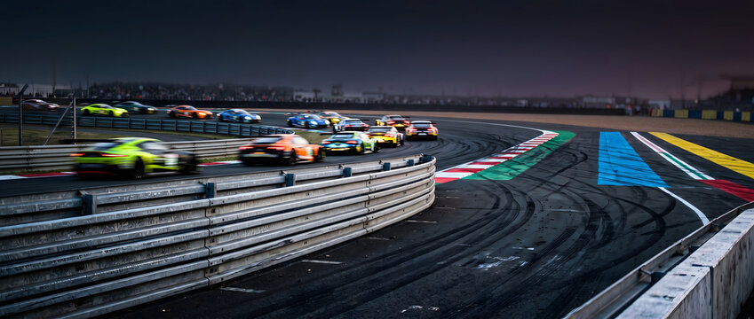 High-speed racing cars navigating a sharp turn on a professional racetrack at dusk with motion blur and vibrant lighting