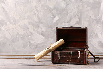 Old chest with treasures, key and map on light wooden table near grunge wall © Pixel-Shot