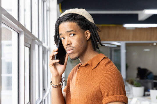 Adult African American man standing by large multi-pane window in modern office, holding smartphone
