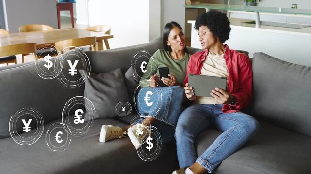Couple at home using phone tablet causing currency icons growing, swirling, fading for finance