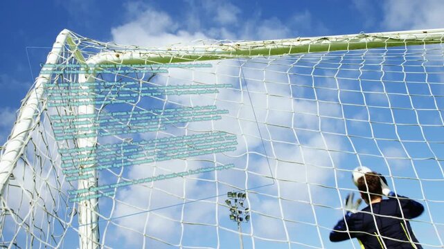 Soccer goalkeeper tracking incoming ball, jumping and reaching gloves over crossbar to stop goal