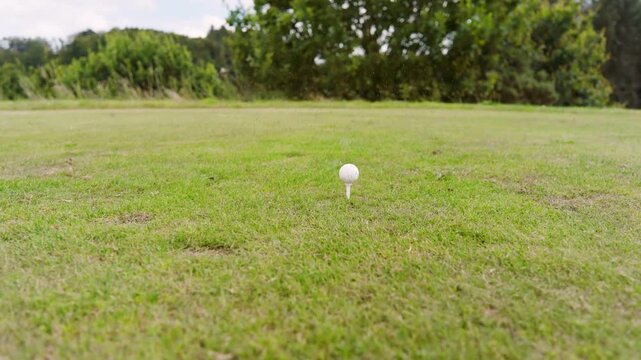 Senior woman placing wooden tee and white ball on grass, aligning driver, swinging for golf shot