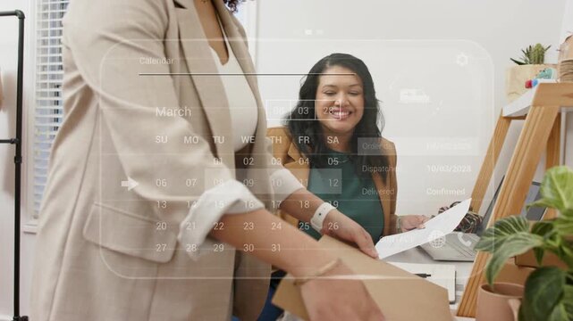 Standing woman bringing box to desk, packing as seated admin checking shipment via calendar HUD