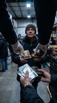 Distribution of luxury food rations in a warehouse setting, with gloved hands passing packaged goods to a man in a beanie, surrounded by shelves and soft lighting